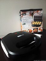 Waffle maker with closed lid beside retail box