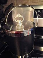 Full view of black metal ice bucket showing handle, lid and polished trim