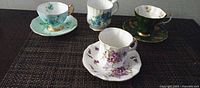 Four bone china drinking pieces displayed: three teacup-saucer sets and one mug