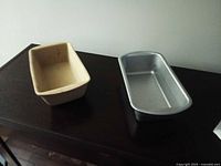 Stoneware and metal loaf pans side by side on table