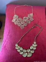Two gold-tone bib necklaces displayed on cushion