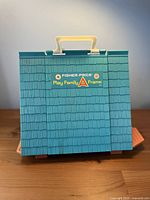 Front view of closed teal A-frame house showing logo and handle