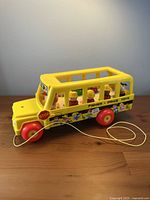 Left side view of yellow Fisher-Price school bus with figures seated inside and pull cord visible