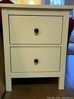 Front view of white two-drawer chest showing knobs and legs