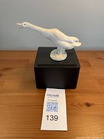Left side view of glossy white porcelain goose figurine on display stand