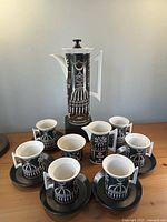 Full coffee service arranged: pot centered on block, six cup-and-saucer settings, creamer and sugar bowl