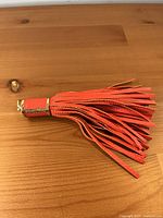 Full view of coral leather tassel charm lying flat
