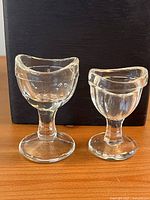 Two clear glass eyewash cups side by side
