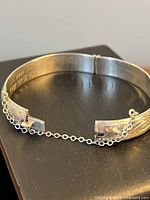 Full view of hinged sterling bracelet showing etched design and safety chain
