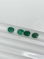 Four oval green emeralds on white background