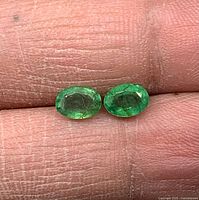 Pair of oval emeralds on fingertip showing size and colour.
