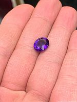 Top view of dark purple oval amethyst gemstone resting on fingers