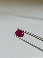 Ruby held by tweezers, showing oval shape and deep red color