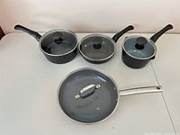 Four black pans and lids laid out on table