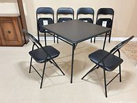 Square black folding table with two chairs opened and four chairs folded behind