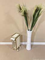 Vase with faux grasses next to wooden stand, full view