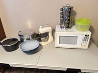 All items arranged on table: microwave, mixer, spice rack, pots, bowls, salad spinner