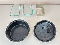 All cookware pieces laid out: two glass loaf pans, one mesh loaf pan, enamel roaster base, lid with perforated trivet
