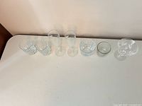 Seven assorted clear glass pieces lined up left to right on table