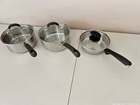 Three stainless steel saucepans with lids, top view showing interiors and handles