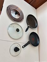 Overhead view of two frying pans and three lids