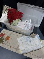 Overview of bin showing various linens including poinsettia placemats, napkins and folded cloths
