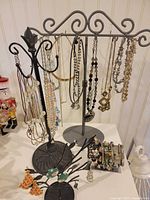 Two scroll-top necklace stands holding various necklaces and background items
