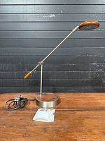 Full view of articulated metal and wood table lamp on wooden surface with power cord visible