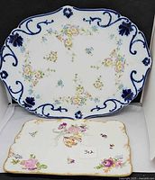 Both porcelain platters showing shapes, floral patterns and relative sizes