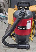 Front view of red Sanitaire backpack vacuum with hose and cord