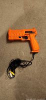 Full view of orange Sega Menacer light gun with attached RCA cables