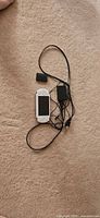 White PSP console, black AC adapter, power cord, detached battery laid on beige surface