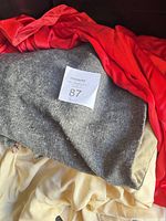 Grey, red and cream capes stacked showing fabrics and colors