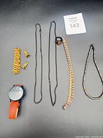 All items laid out: watch, copper necklace, black ring, black chains, copper bracelet, gold parts