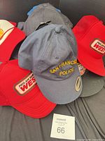 Pile of hats highlighting navy "San Francisco Police" cap and red "Pro-Am Series West" trucker hats