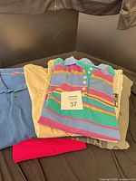 Stack of folded shirts and pants showing multicolor polo, beige pants, grey and pink T-shirts