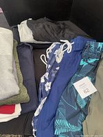 Overview of folded garments including swim trunks with tags and assorted tops