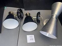 Two black wall sconces and one silver double-cone sconce laid on table