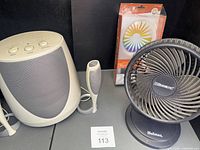 Overall lot showing Harman/Kardon subwoofer, satellite speaker, OttLite magnifying glass package and Holmes fan