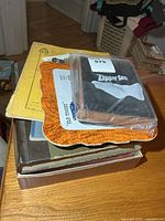 Stack of assorted manuals including sealed "Zipper Sea" booklet, yellow manual, orange-bordered booklet, brown binder