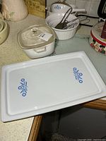 Top view of rectangular Corning Ware tray with Cornflower motif; accompaniment of square casserole with lid, two round dishes, metal handles visible