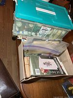 Plastic tote with teal lid stacked on cardboard box of craft items