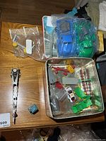 Tin opened showing assorted Marx plastic playset parts, metal girder track, blue cube
