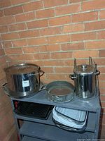Shelf holding stainless stock pot, springform pan, pasta cooker set, stacked baking and grill pans