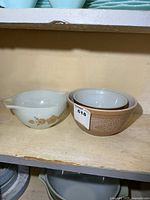 Three Pyrex bowls on shelf: white Butterfly Gold Cinderella bowl and two nested brown Woodland bowls