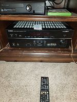 Front view of Yamaha RX-V671 receiver on shelf with remote on carpet