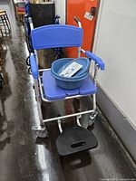 Front view of blue aluminum rolling commode/shower chair with bucket placed on seat