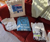 Four event T-shirts on sofa: best Cancer Walk, Run for NH 10-Mile, Boston’s Run to Remember, additional cream shirt edge