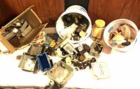 Tabletop view of scattered metal boxes, blue plastic box, receptacles, switches, lamp sockets, buckets and jar containing wire nuts