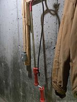 Full view of red-handled drain snake hanging on wall